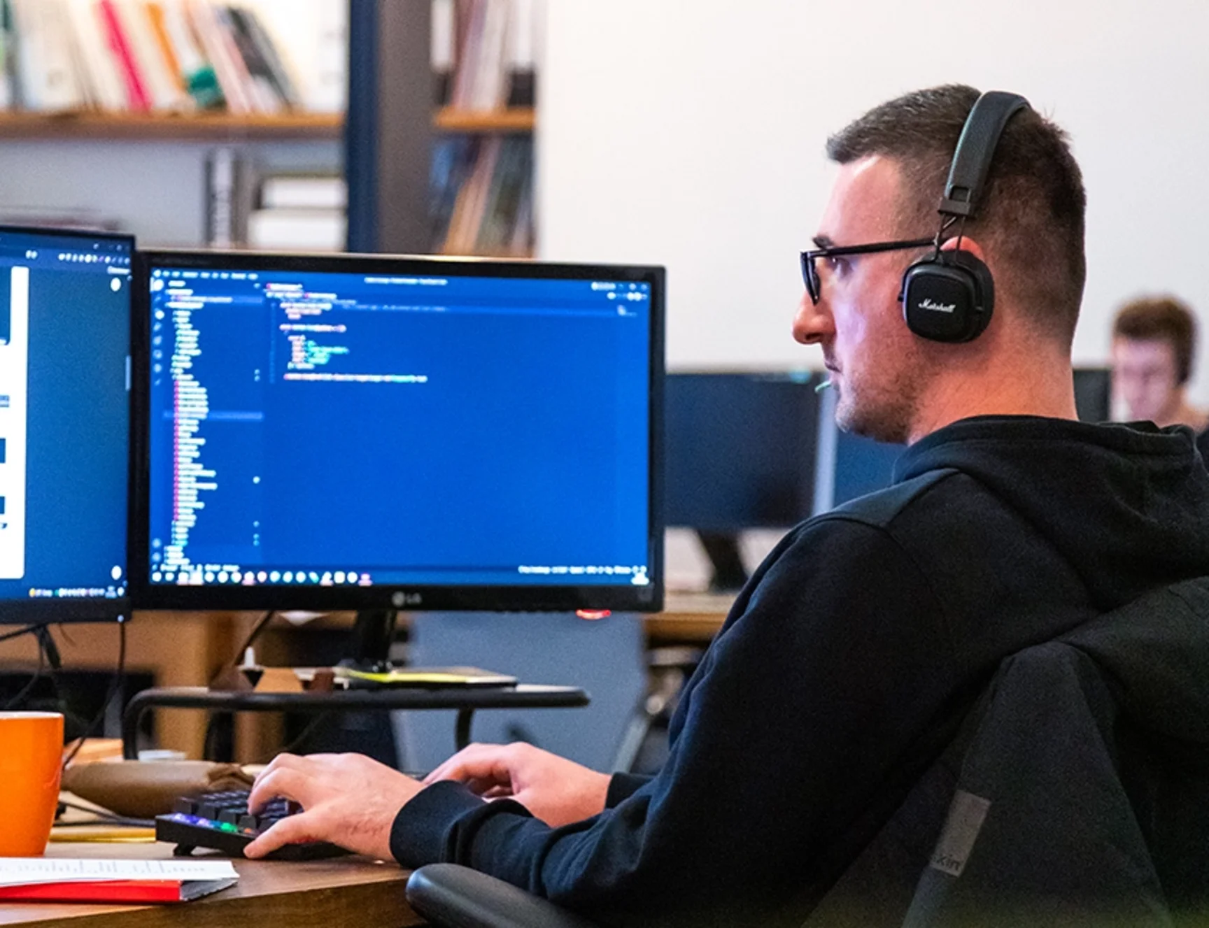 DER PUNKT-Mitarbeiter arbeitet an mehreren Monitoren an der Entwicklung einer Website.